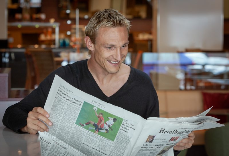 Sami Hyypiä lukee sanomalehteä hymyillen